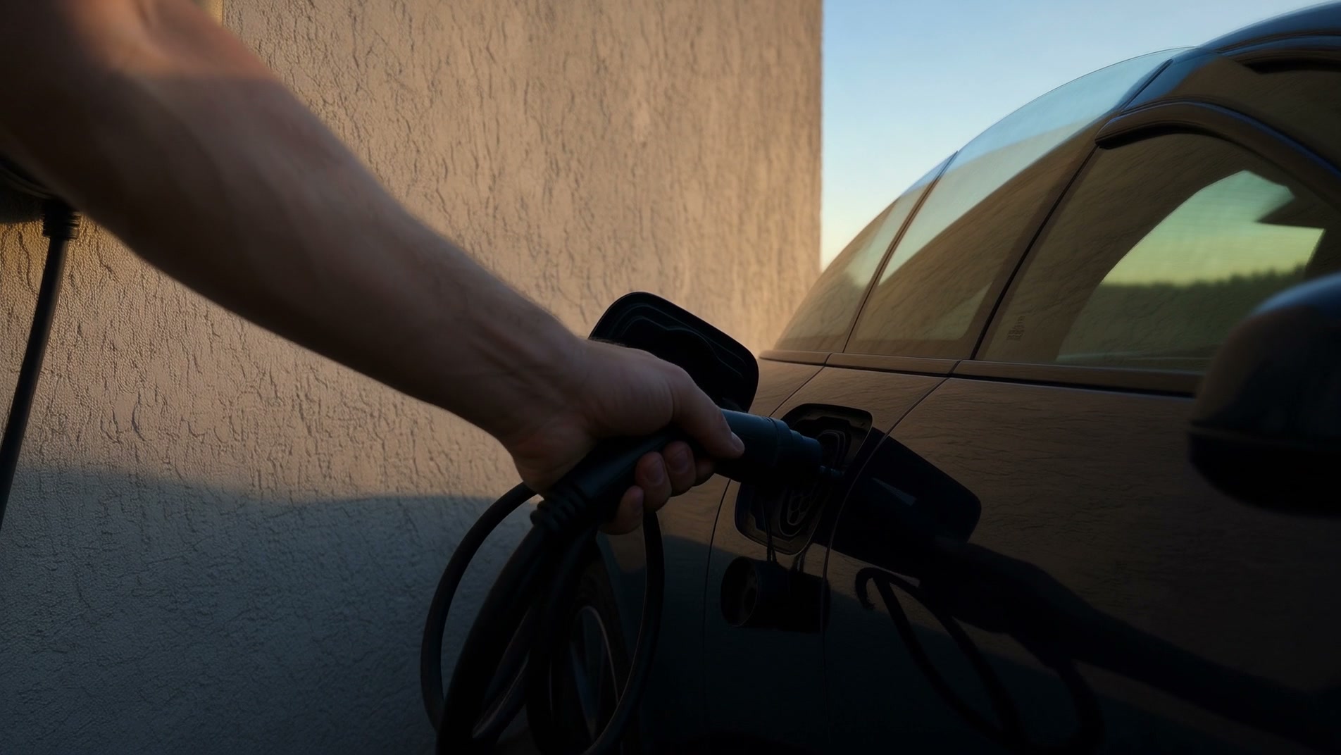 Wallbox mit Ladekabel neben einem Elektroauto in der Einfahrt